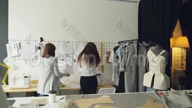 年轻的企业家服装设计师站在墙前挂着草图，讨论图纸和放置